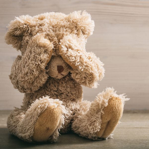 Child abuse concept. Teddy bear covering eyes in an empty room